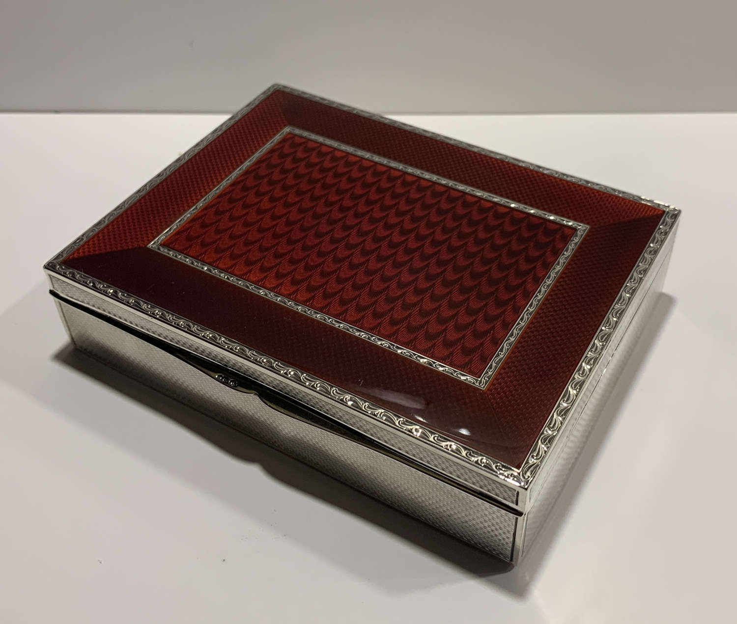 A sterling silver and blood red guilloche enamel cigar / cigarette box